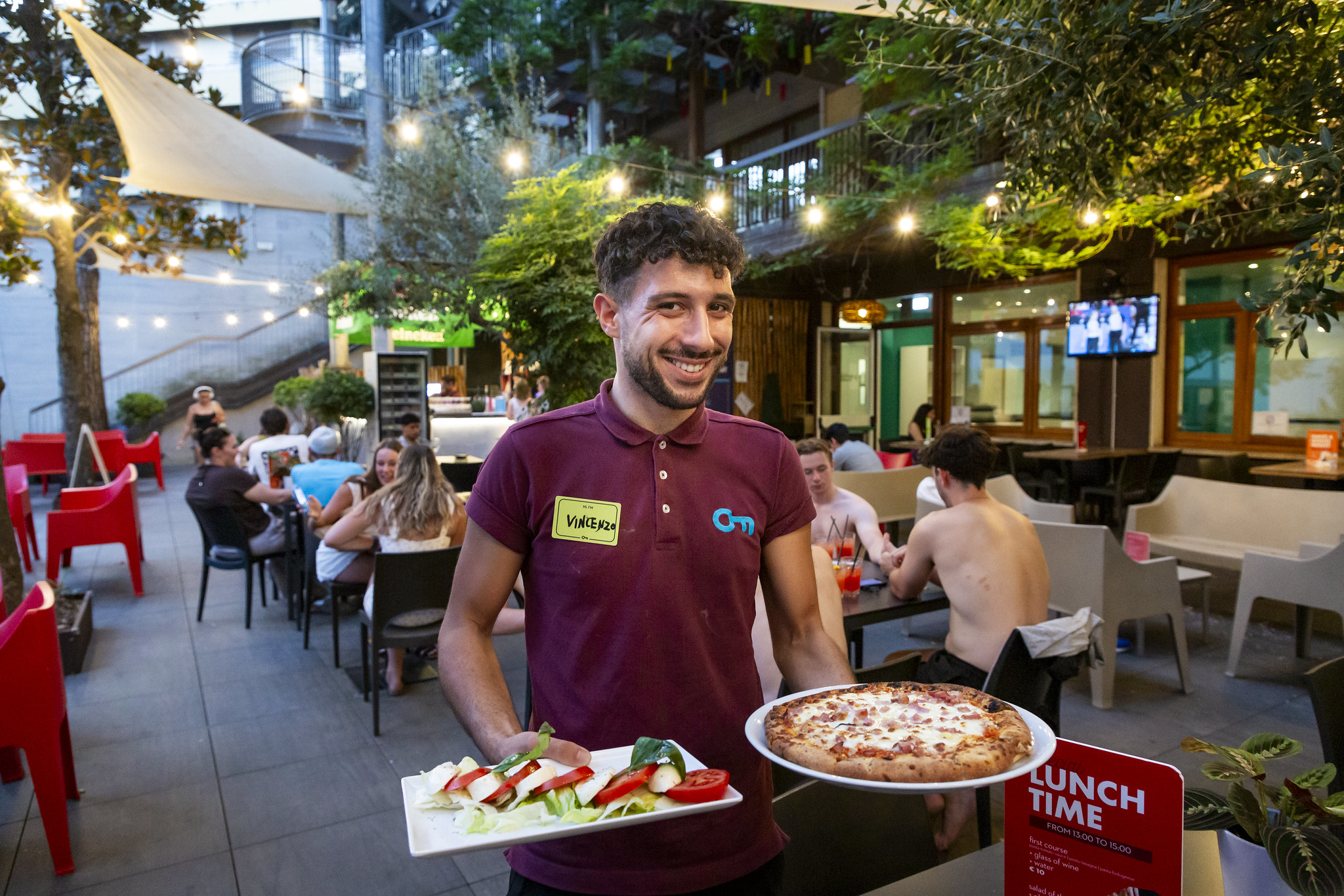 Cameriere che porta una pizza e un'insalata caprese